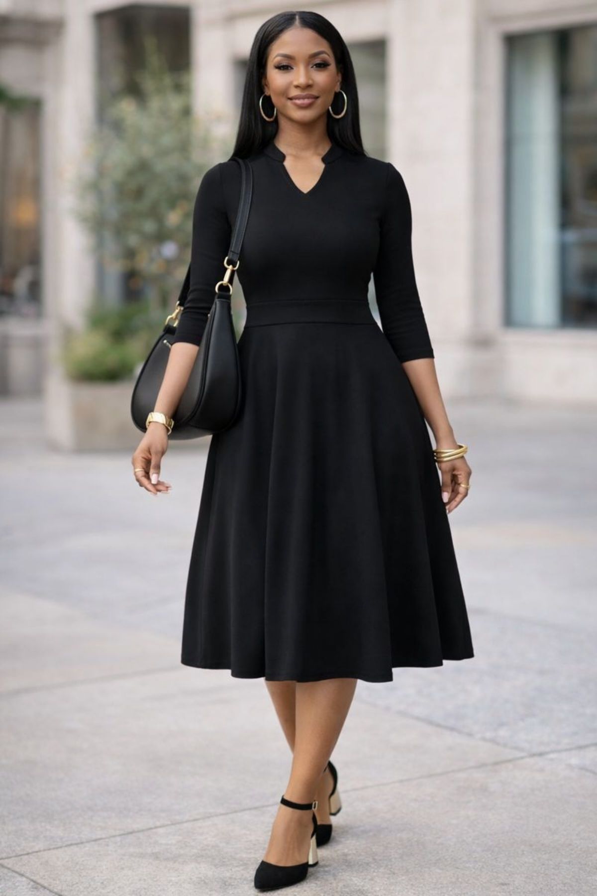 Woman wearing a classic black midi dress with three-quarter sleeves, styled with black heels and a black shoulder bag, walking confidently in a city setting.