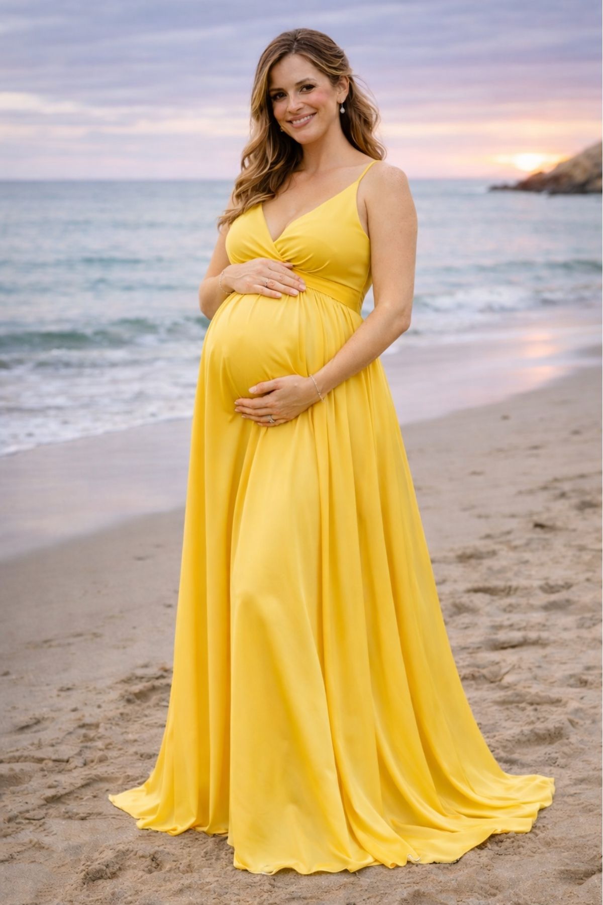 Pregnant bridesmaid in a bright yellow flowing dress at a beach wedding during sunset.