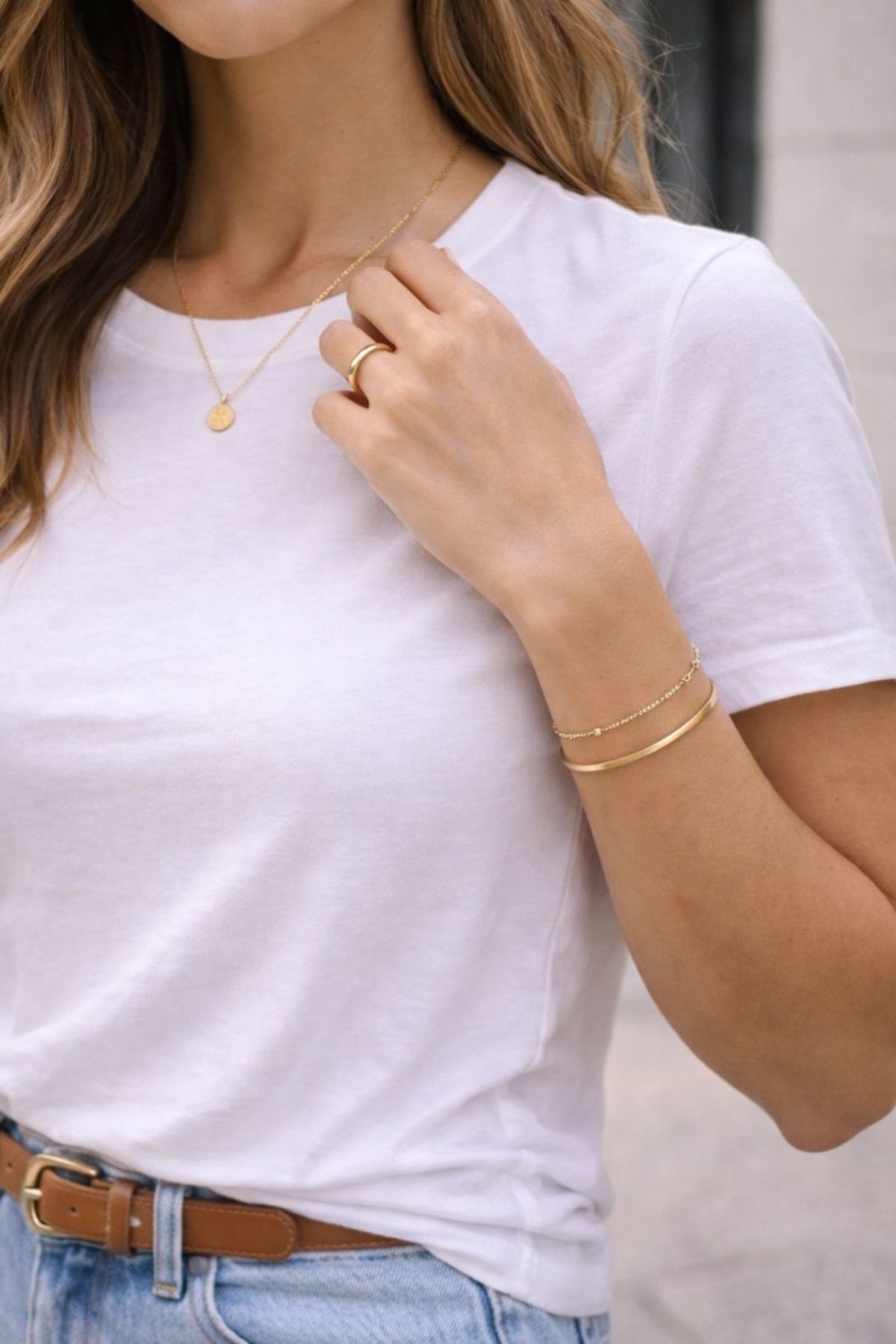 Close-up of minimal gold jewelry including a delicate necklace, bracelet and ring styled with a white T-shirt, adding subtle elegance to a casual everyday outfit.