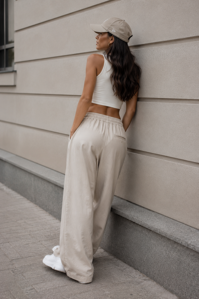 Woman in wide-leg beige pants, a white crop top and sneakers creating a comfortable girl-next-door style look.